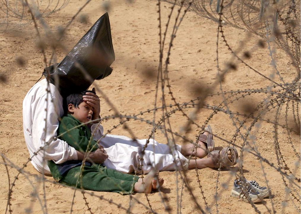 Un prisionero iraqu&iacute; internado en un campo de detenci&oacute;n durante la Guerra de Iraq (2003-2011), desencadenada intelectualmente por los neoconservadores estadounidenses durante el mandato de George W. Bush, consuela a su hijo de cuatro a&ntilde;os capturado con &eacute;l, Nayaf, Iraq, 31 de marzo de 2003 - Aljazeera, Jean-Marc Bouju / AP Photo.
