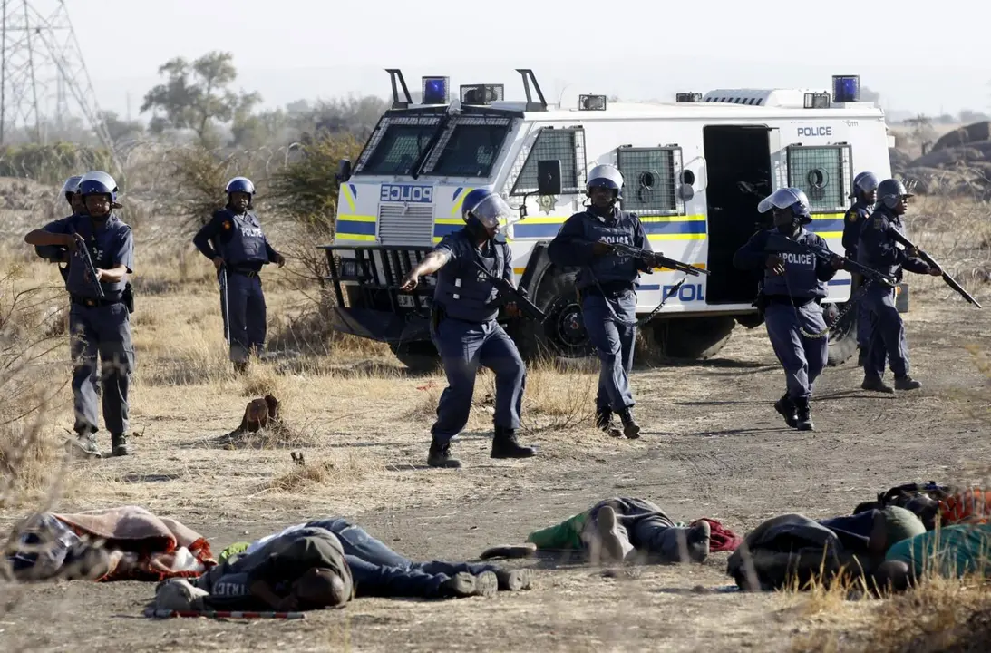 Un polic&iacute;a gesticula frente a los cuerpos de algunos de los treinta y cuatro mineros asesinados el 16 de agosto de 2012 por la polic&iacute;a sudafricana en la mina de platino de la empresa Lonmin situada en Marikana (Rustenburg, North West Province), durante la presidencia de Jacob Zuma. El director de Lonmin, adem&aacute;s de accionista de la empresa, en ese momento era Cyril Ramaphosa, actual presidente de Sud&aacute;frica &ndash; South African History Online / Siphiwe Sibeko.