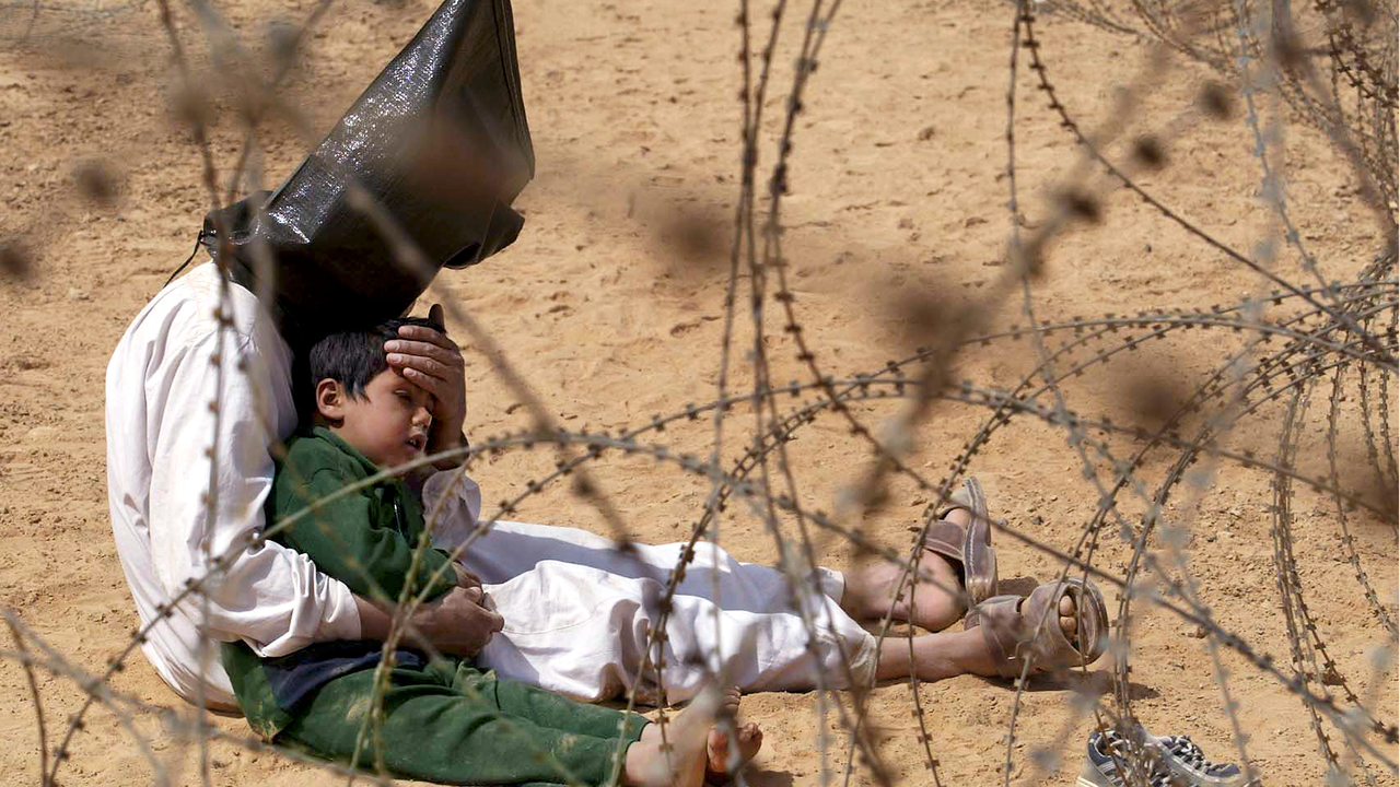 Un prisionero iraqu&iacute; internado en un campo de detenci&oacute;n durante la Guerra de Iraq (2003-2011), desencadenada intelectualmente por los neoconservadores estadounidenses durante el mandato de George W. Bush, consuela a su hijo de cuatro a&ntilde;os capturado con &eacute;l, Nayaf, Iraq, 31 de marzo de 2003 - Aljazeera, Jean-Marc Bouju / AP Photo.